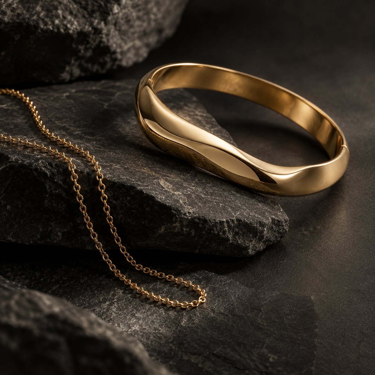 Goldener Armreif und Kette auf dunklem Stein